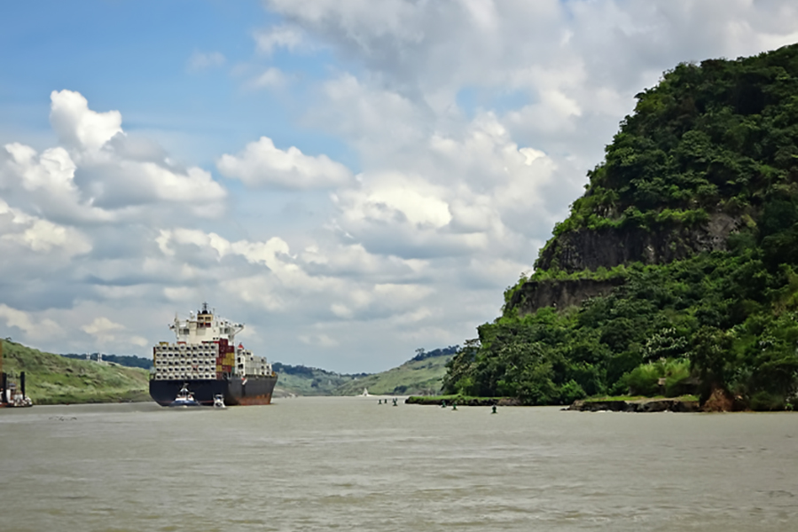 A cargo ship navigates the Panama Canal, flanked by the rainforest